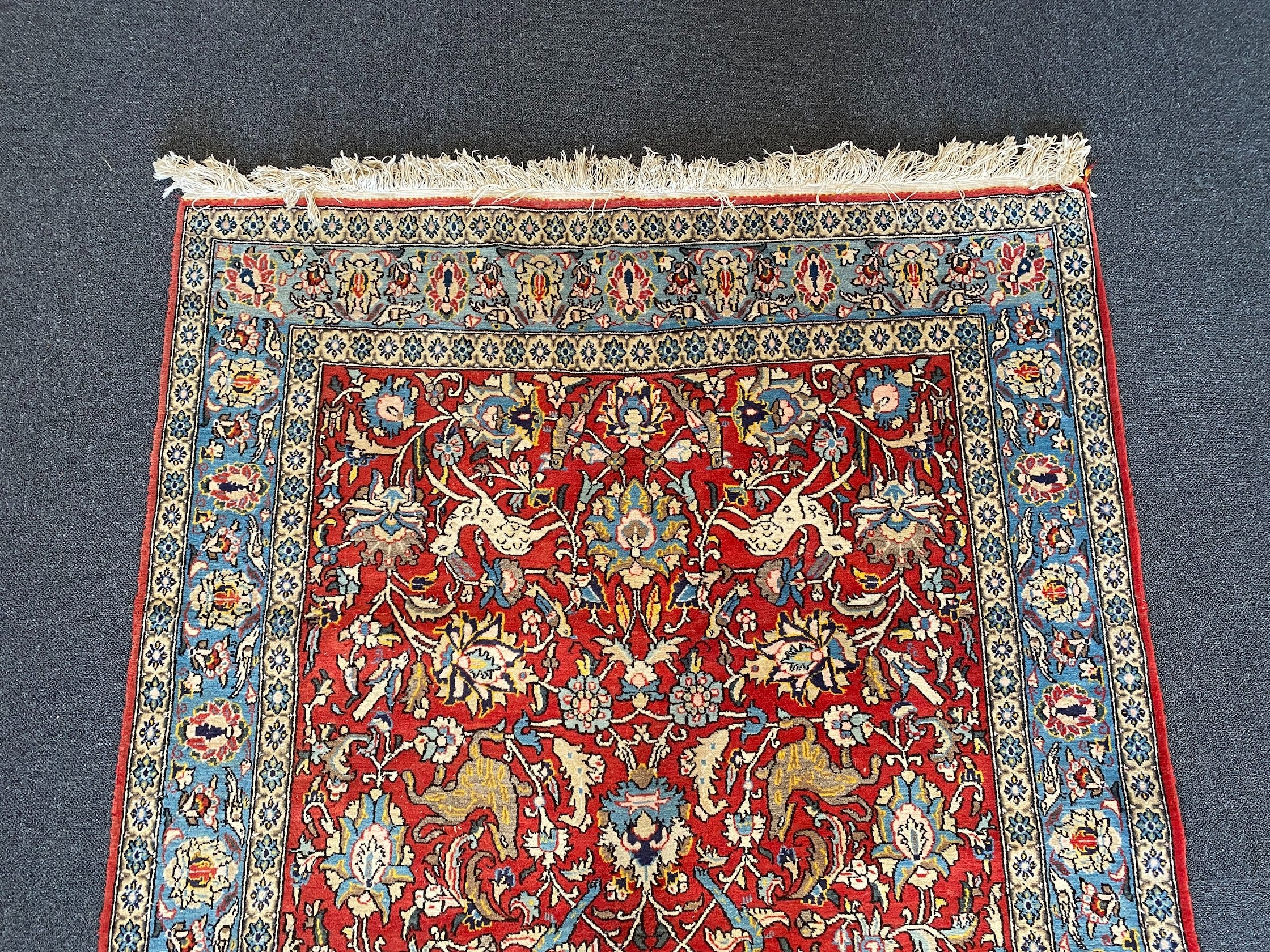 A Persian Qum red ground rug woven with animals and exotic birds among stylised flower heads 220 x 125 cms